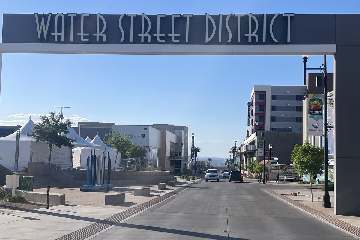 The Water Street District gateway sign arching over the roadway in downtown Henderson, Nevada, with two vehicles heading south toward the valley on a clear morning